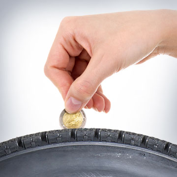 Hand prüft Reifenprofil mit Münze